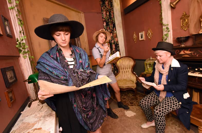 Costumed players studying clues in an escape room parlor